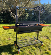 Barbacoa argentina profesional Dalí de Wagner Grills con doble bandeja lateral de madera, sistema de elevación por manivela y diseño robusto en negro.
