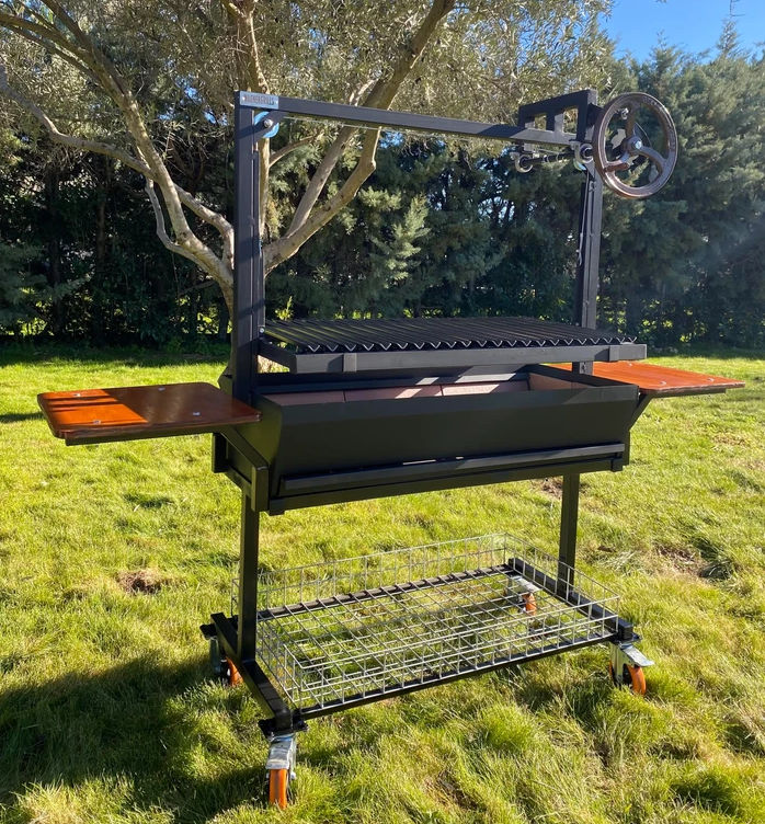 Barbacoa argentina profesional Dalí de Wagner Grills con doble bandeja lateral de madera, sistema de elevación por manivela y diseño robusto en negro.