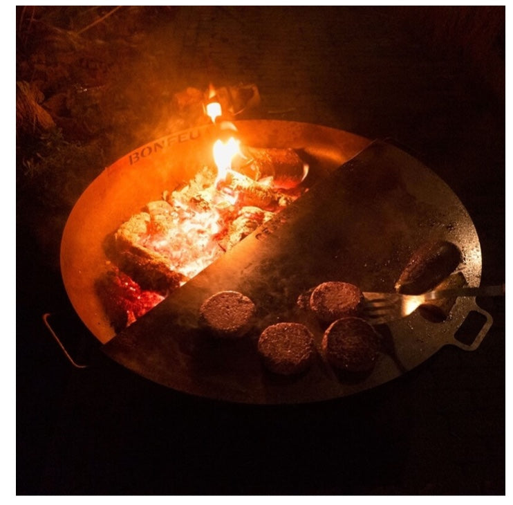 Cocinando hamburguesas de noche en un brasero BonFeu con la media plancha iluminada por el fuego.