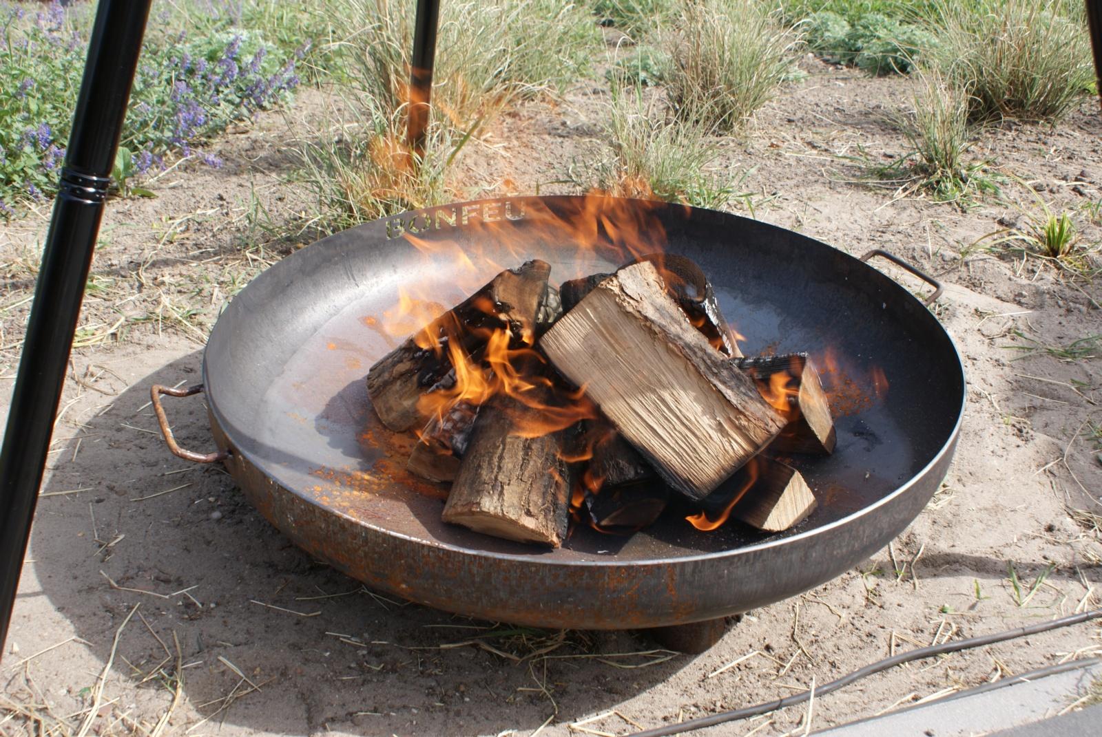 Brasero BonBowl Plus en el suelo encendido con leña para calor de exterior.