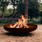 Brasero de diseño bajo BonFeu Jesco en acero corten con fuego de leña en el jardín.