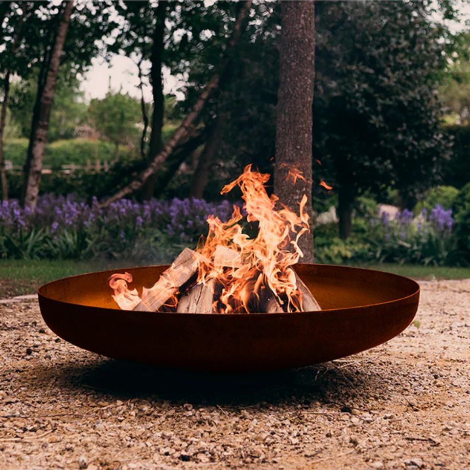 Brasero de diseño bajo BonFeu Jesco en acero corten con fuego de leña en el jardín.