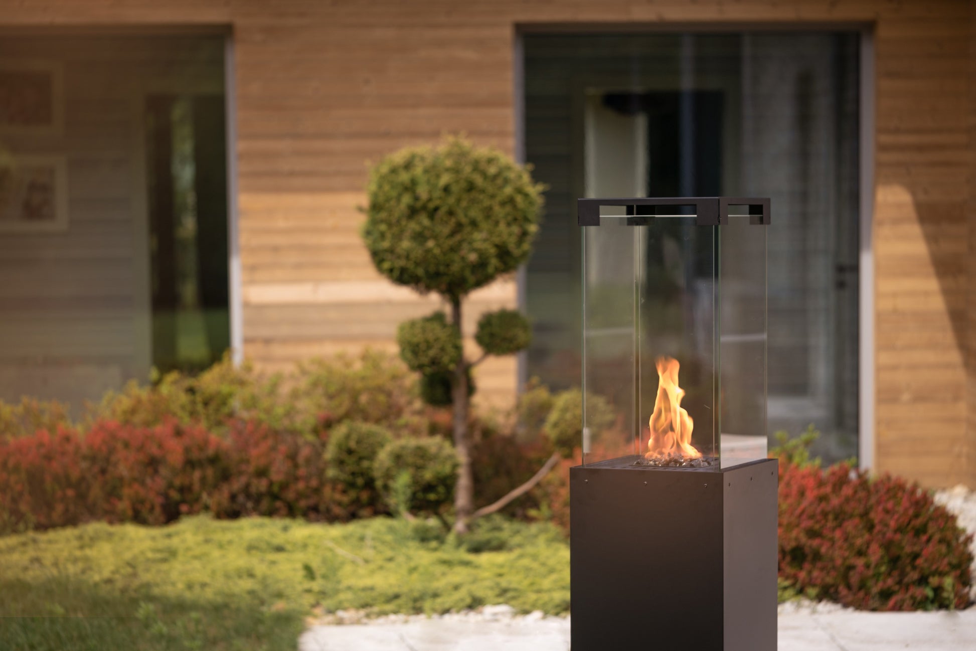 Estufa Planika Faro encendida en un jardín moderno proporcionando calor y ambiente