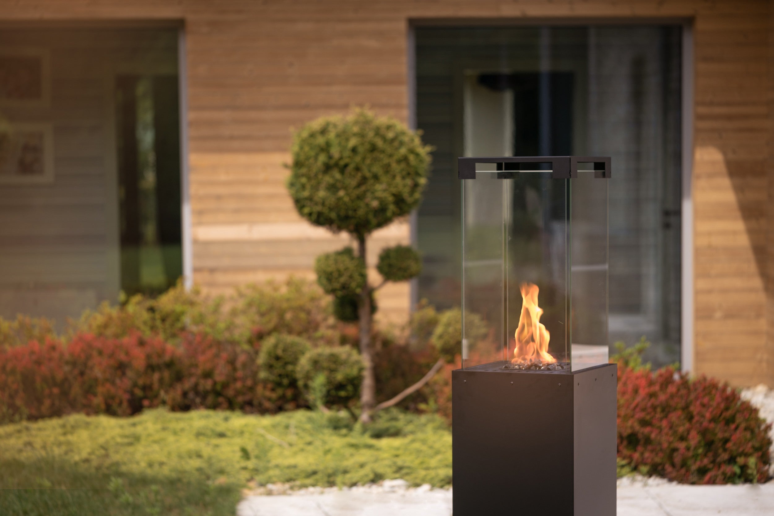 Estufa Planika Faro encendida en un jardín moderno proporcionando calor y ambiente