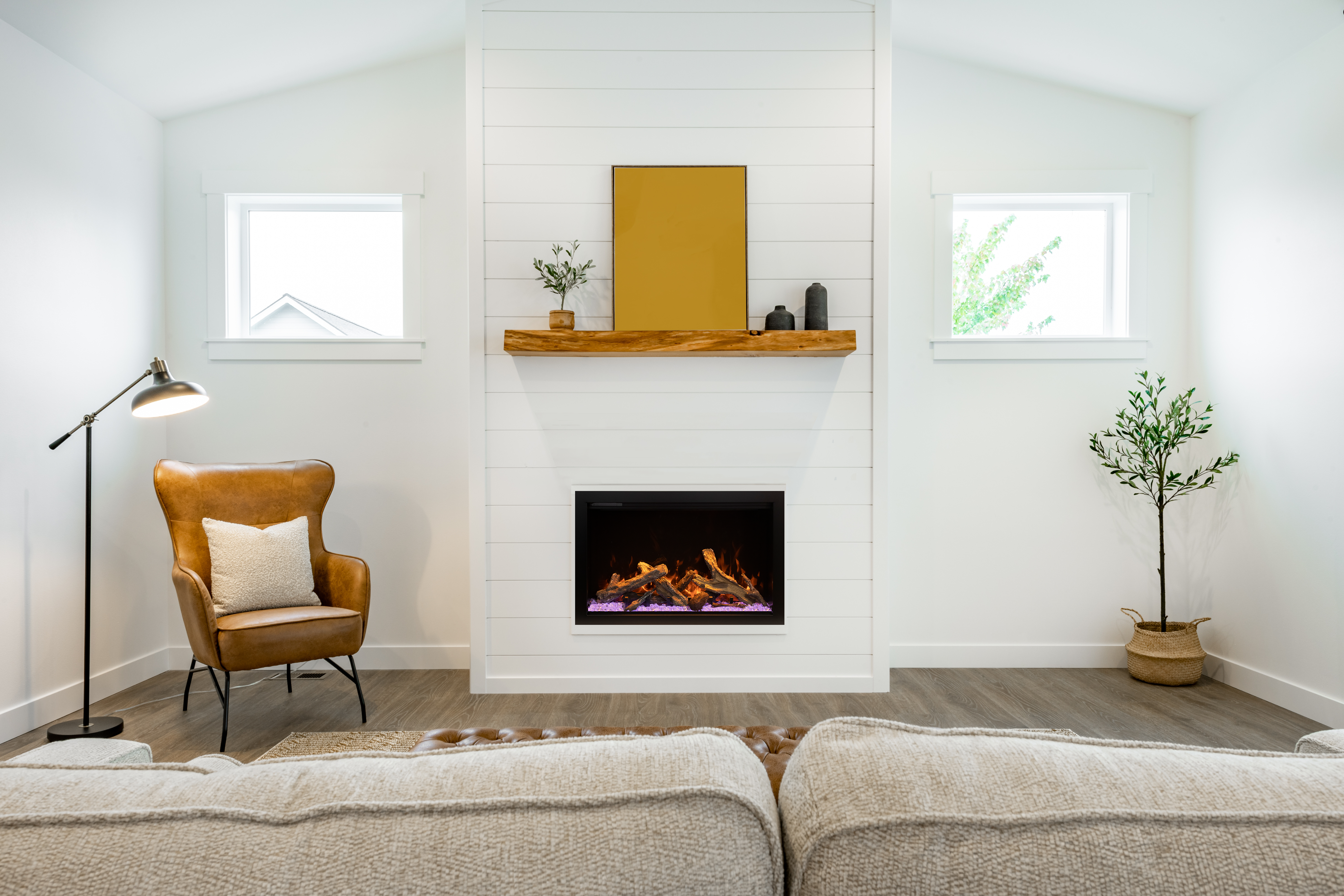 Chimenea eléctrica Amantii TRD Bespoke integrada en pared blanca con estante de madera y sillón de cuero