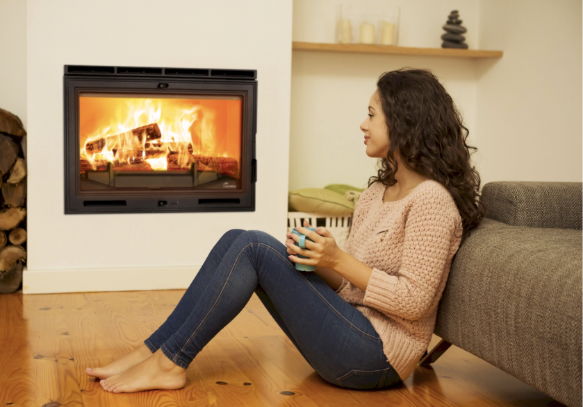 Mujer relajada junto a una chimenea de leña Lacunza IN 700 encendida en un salón acogedor
