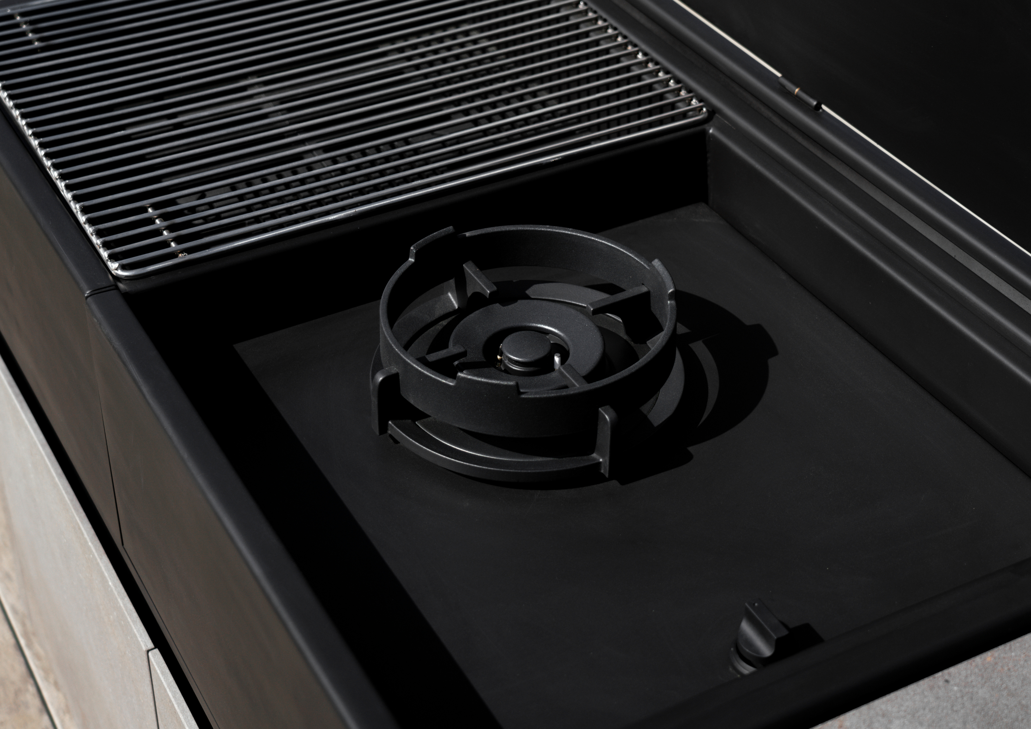 Detalle del firepit integrado en la cocina de exterior Rekker K7 para crear un ambiente cálido en la terraza.