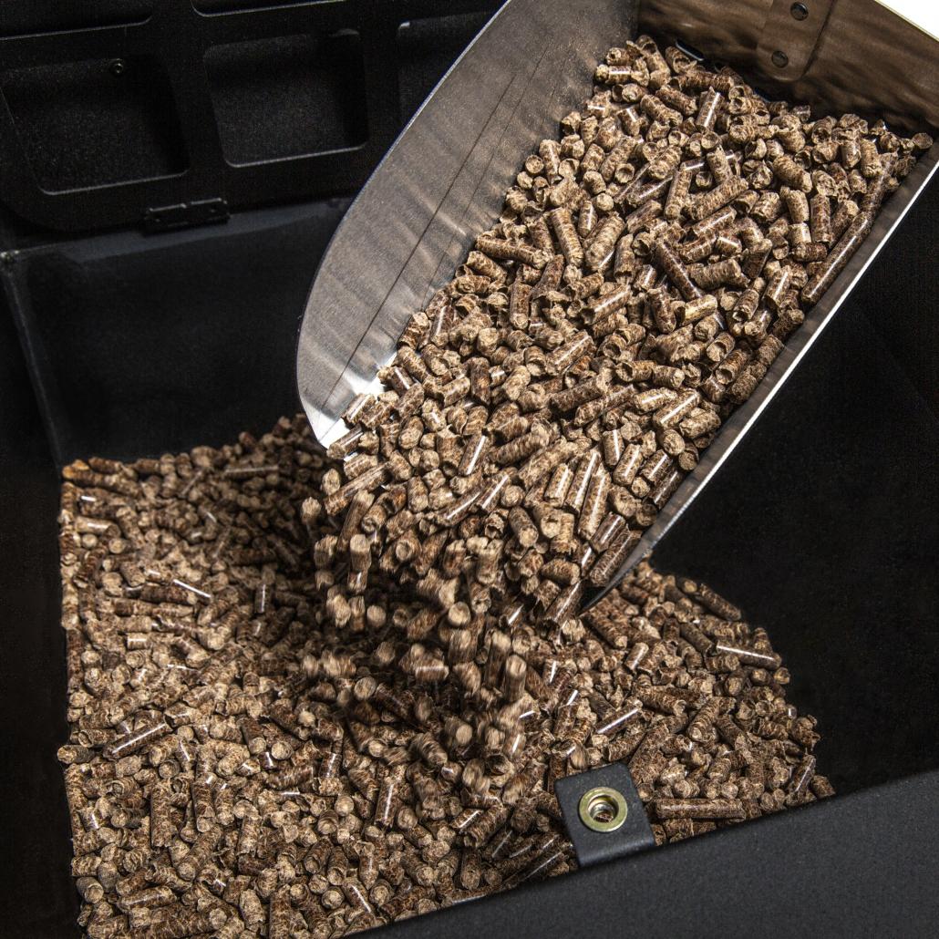 Detalle de la tolva de gran capacidad de la barbacoa Broil King Regal Pellet 500 siendo cargada con pellets de madera