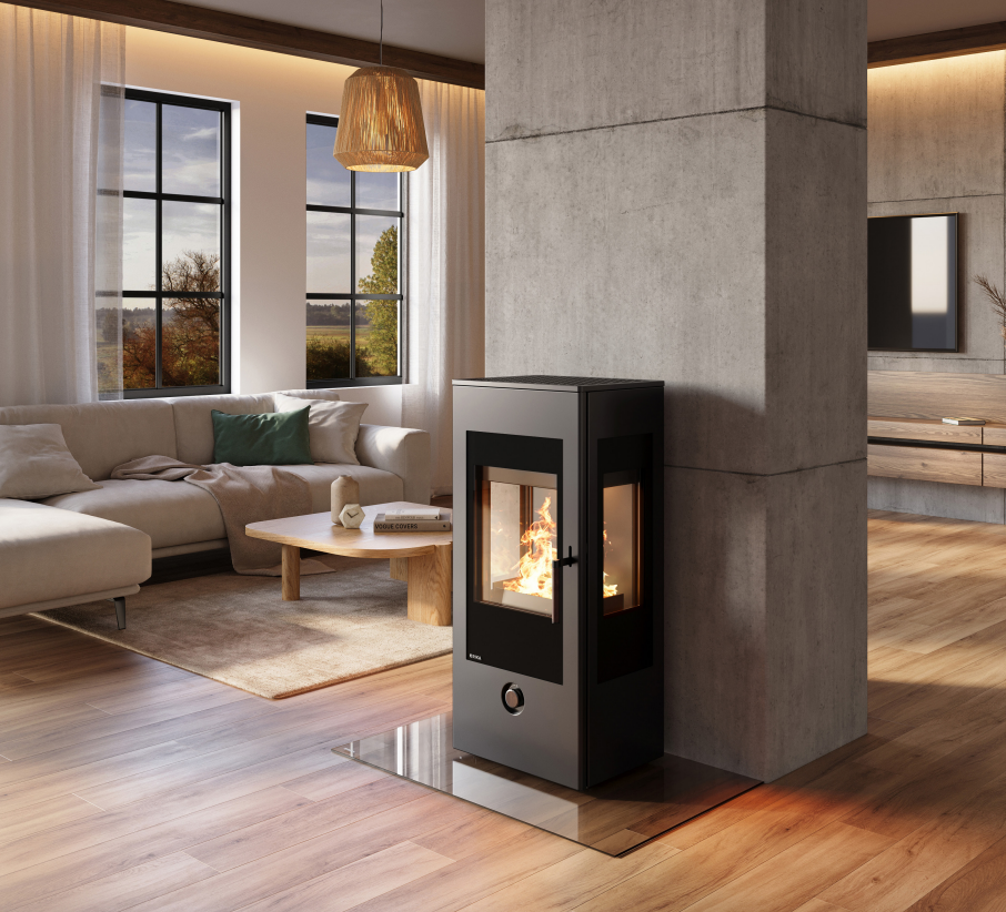 Estufa de leña Rika Trio con triple cristal instalada junto a una columna de hormigón en un salón de diseño industrial
