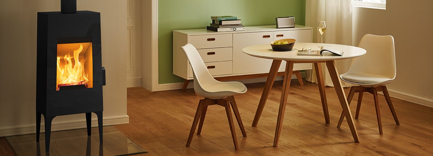 Estufa Rika Look con base de madera integrada en un comedor nórdico, resaltando la calidez del hogar y el diseño contemporáneo