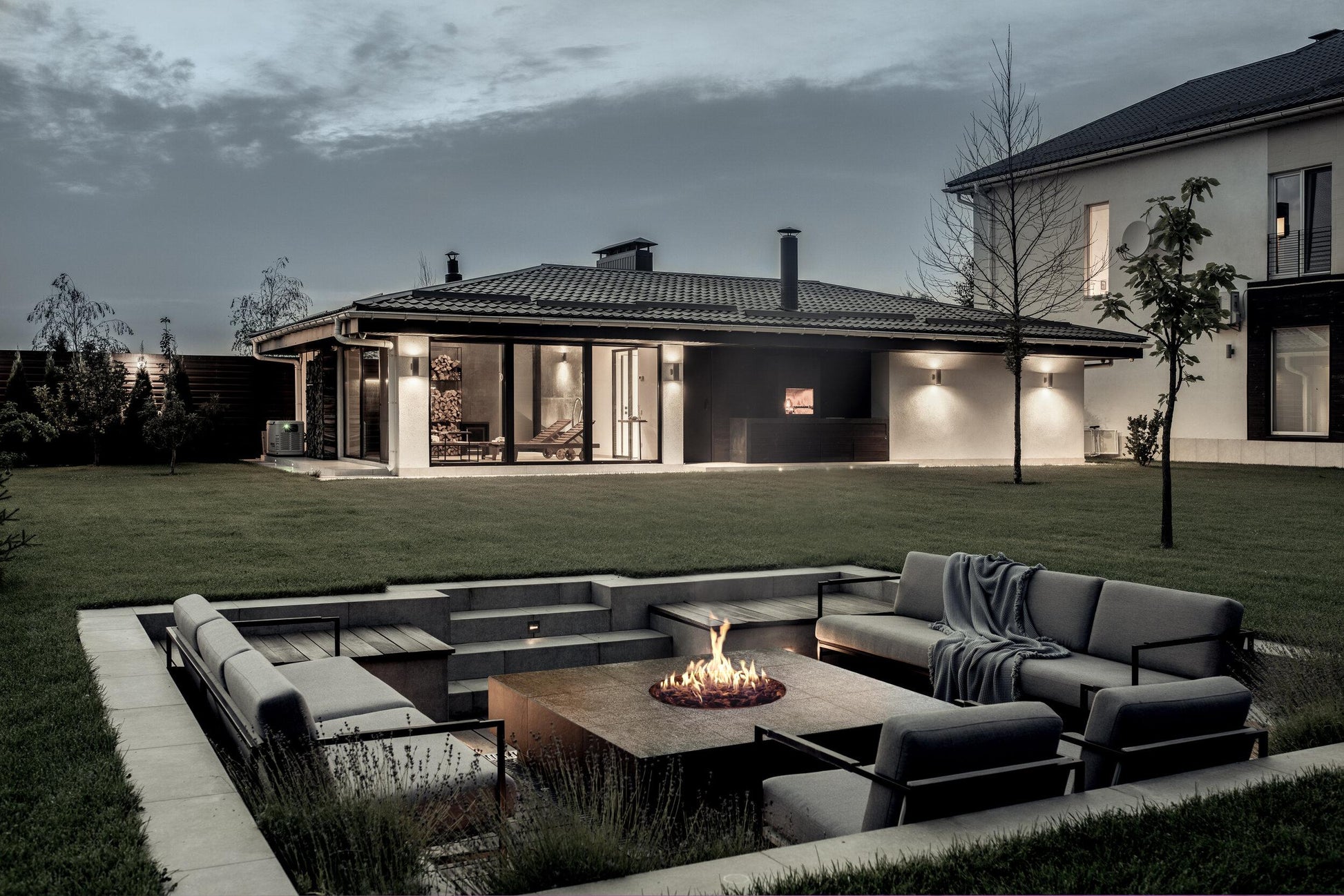 Zona de fuego exterior circular con quemador Galio Star de Planika en un jardín de diseño nocturno