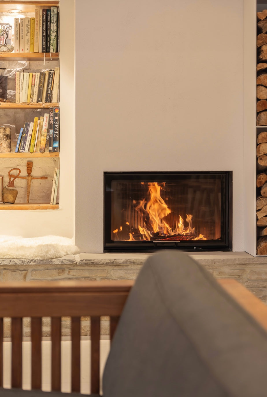 Hogar de leña Hoxter Haka 78/57 instalado en una chimenea moderna con revestimiento de obra y zona de lectura.