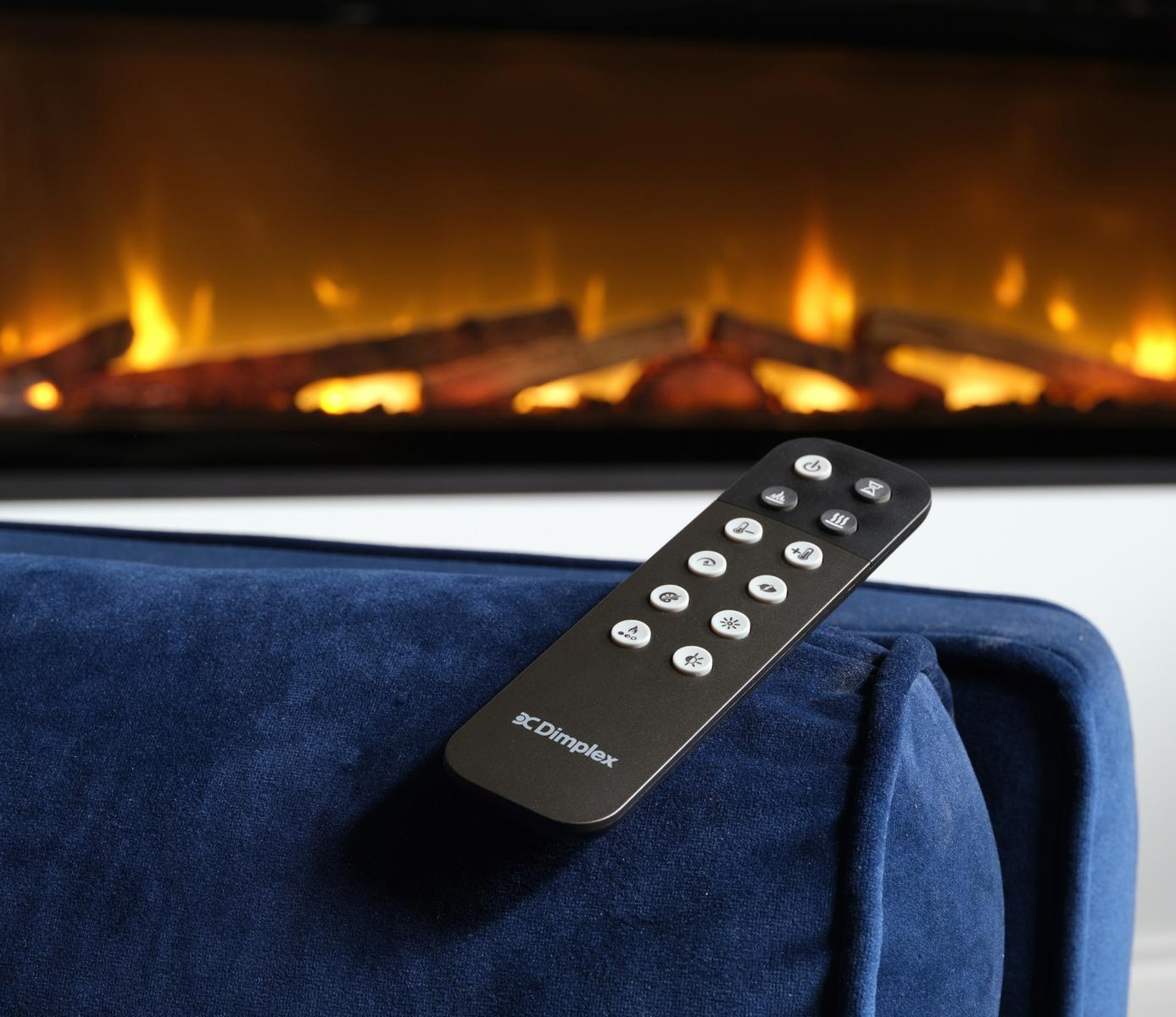 Mando a distancia ergonómico sobre sofá azul para controlar la chimenea Dimplex Night Evolve
