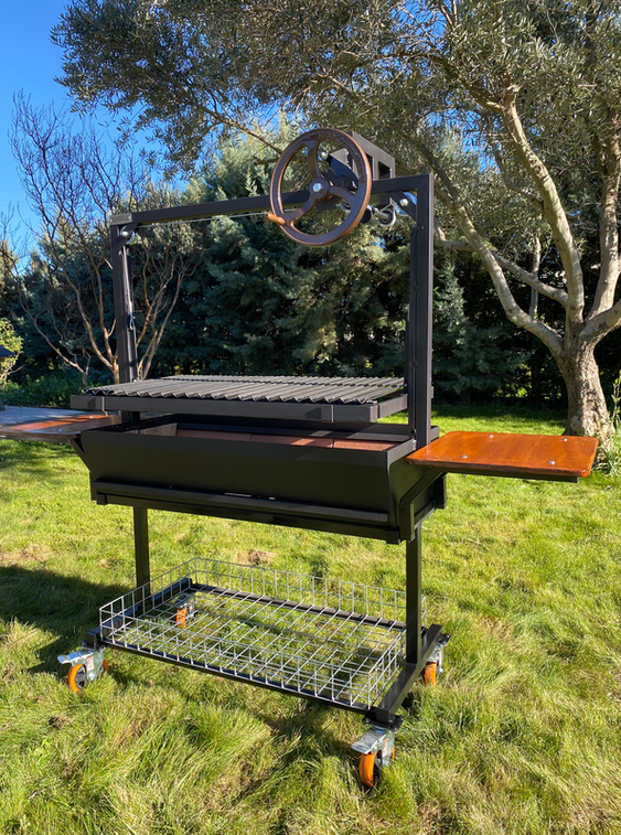 Parrilla argentina Dalí con bandejas laterales de madera para preparación, estructura de acero reforzado y ruedas industriales para fácil movilidad