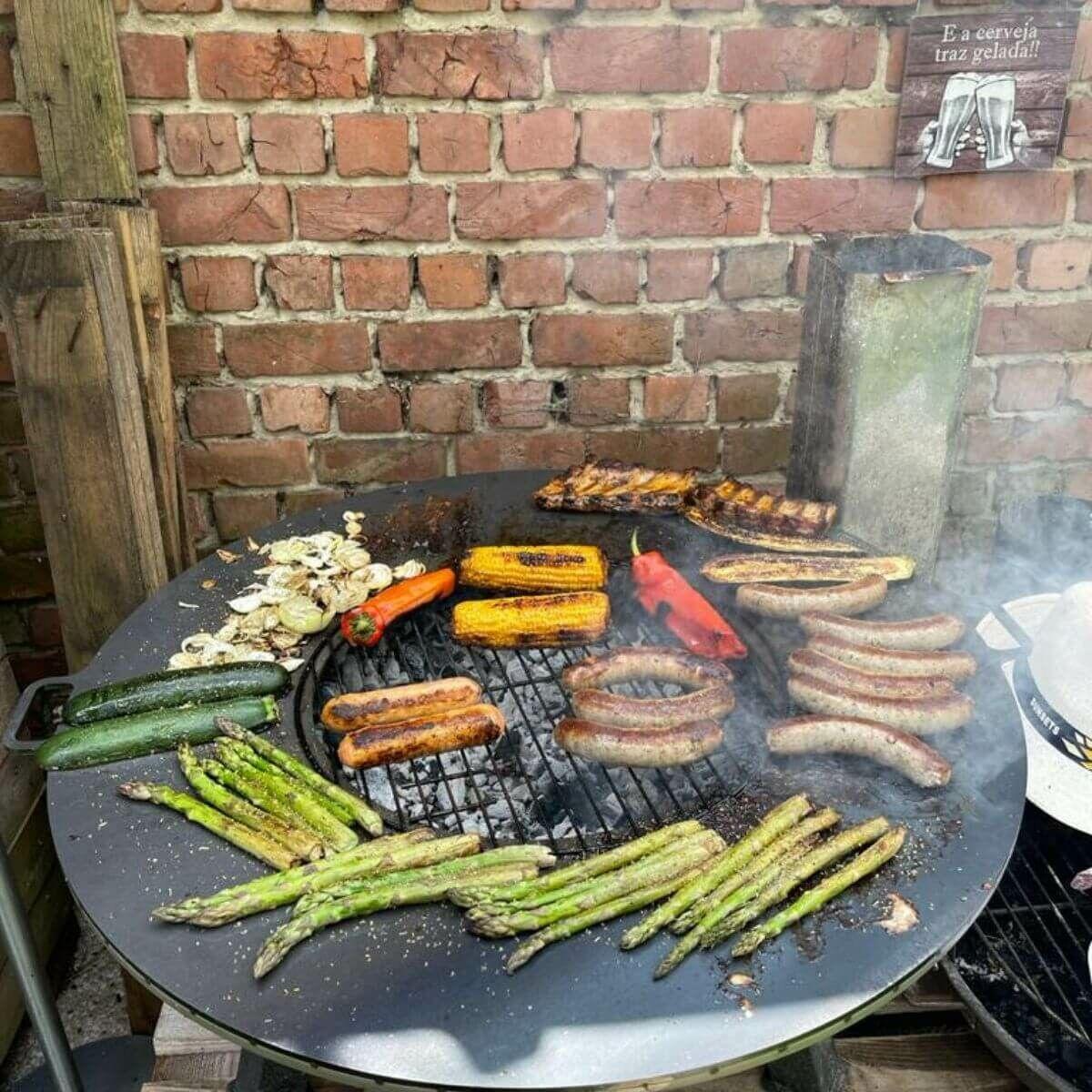 Vista superior de la gran superficie de cocinado del brasero BonFeu con espárragos y carne.